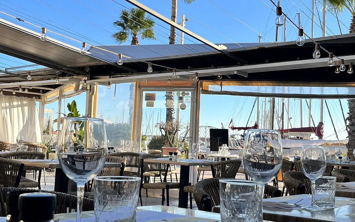 La terrasse de Chez Marcel en journée, face au port de plaisance et aux palmiers