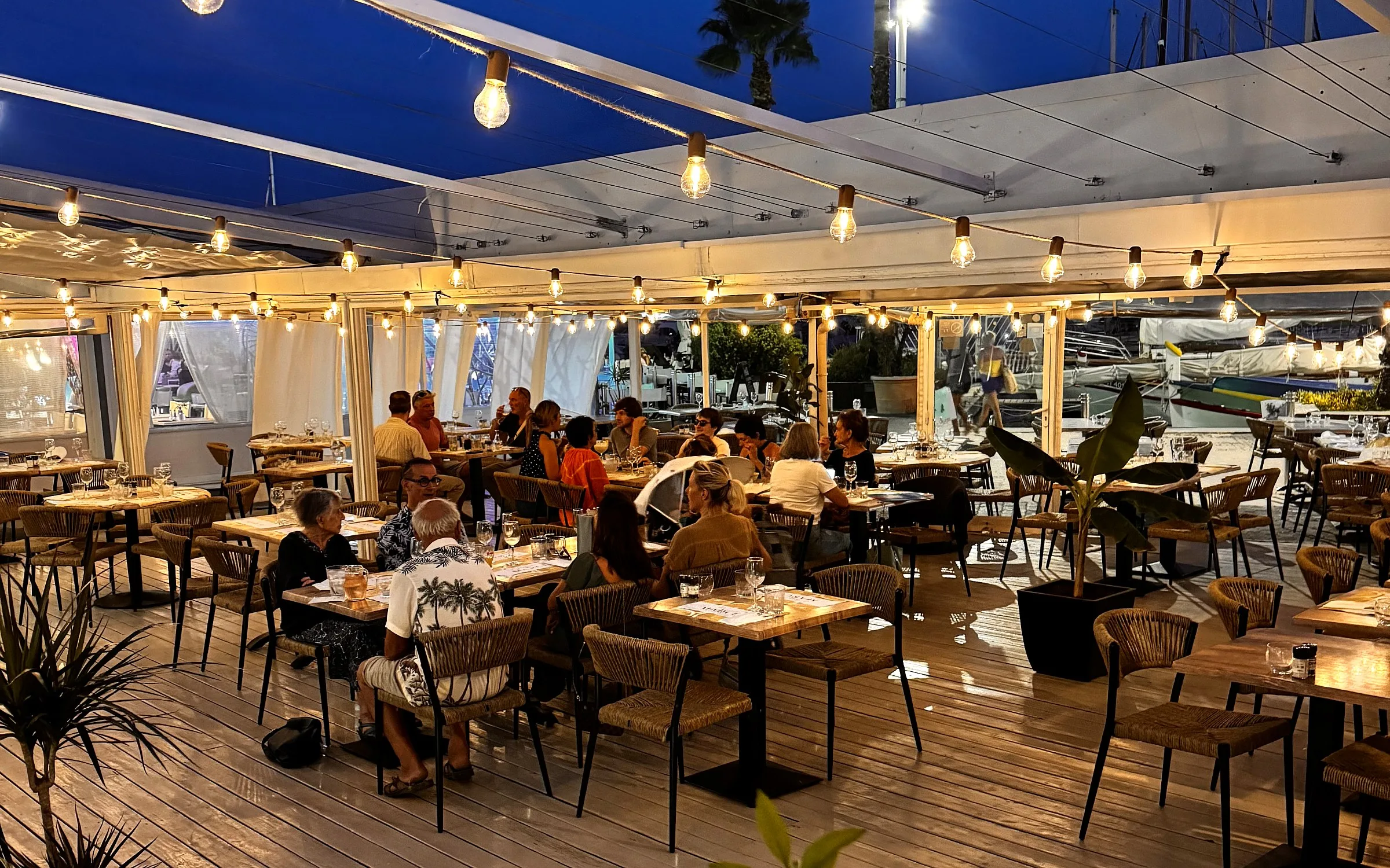 La terrasse de Chez Marcel illuminée de guirlandes à la tombée de la nuit, face au port de Palavas-les-Flots